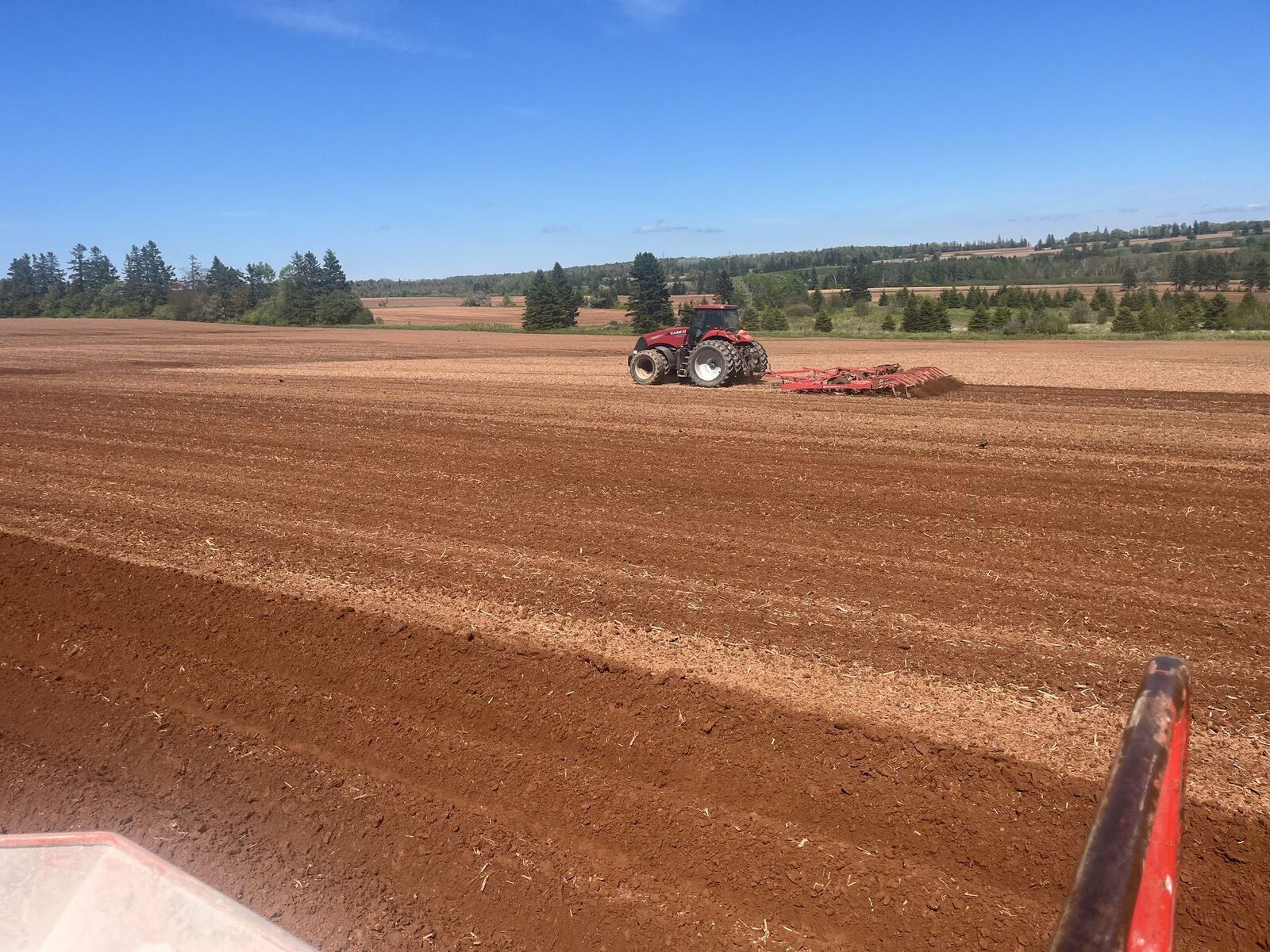 A tractor working a wide red-soil field on Prince Edward Island's south shore